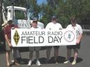Left to right, the Gang of 4: John KX7YT/S21YV, Jerry K7VIT, Chris N7UBS (GOTA), and John N7AAM display their ARRL/ARES/Field Day banner (and pride) while standing in front of a mighty fine "antenna support structure."   Photo courtesy of Christine, XYL of KX7YT/S21YV.
